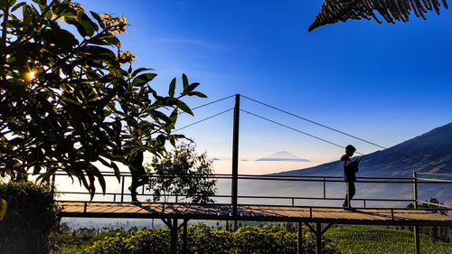 Young man standing on footbridge against sky