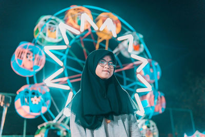 Portrait of young woman standing against illuminated lighting equipment