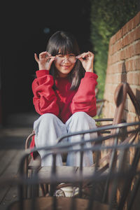 Cheerful asian teenager wearing eyeglasses sitting on wood desk