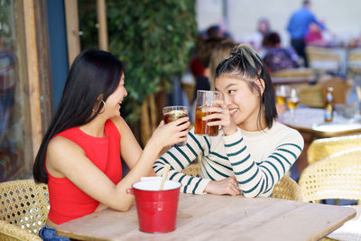 Smiling friends using mobile phone while sitting at restaurant