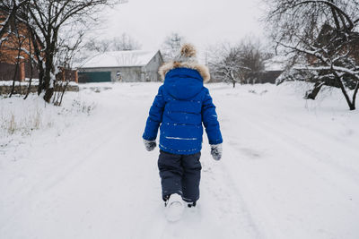 Best outdoor winter activities for kids. back view kid boy in blue winter jacket walking down a