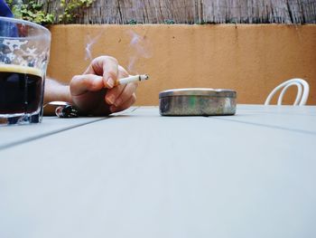 Cropped hand of man holding cigarette by tea at table