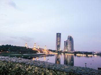 Illuminated buildings by river against sky in city