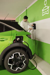 Man plugging cord to charge electric car at charging station