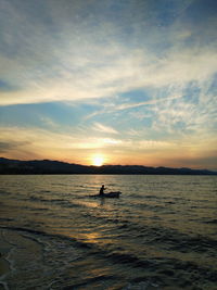 Silhouette person in sea against sky during sunset