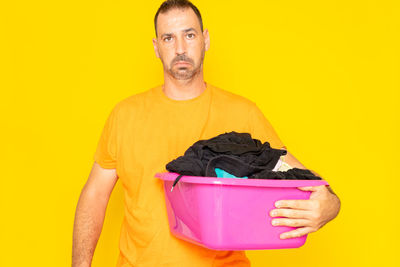 Portrait of young man holding bucket while standing against yellow background