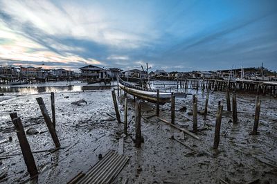 Wooden posts on pier amidst buildings against sky during winter