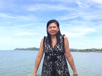 Portrait of smiling woman standing in sea against sky