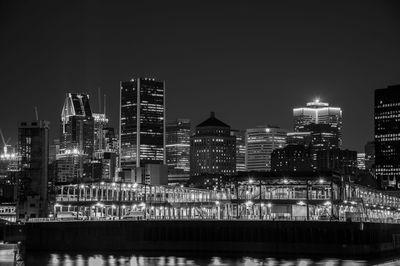 Illuminated buildings by river against sky at night