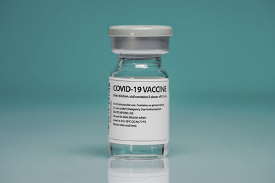 Medical glass vial with coronavirus vaccine placed against blue background