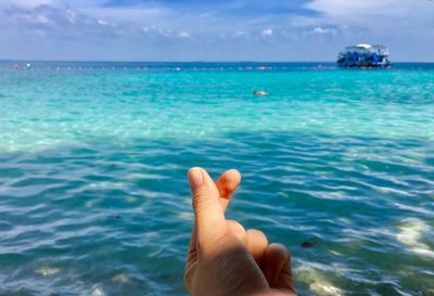 Close-up of hand over sea against blue sky