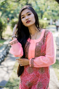 Beautiful young woman standing against pink background