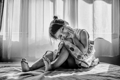 Cute girl sitting on bed against window at home