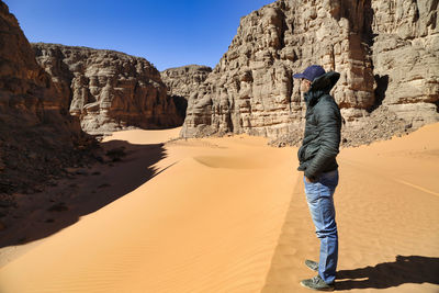 Side view of man standing on sand at desert against clear sky during sunny day