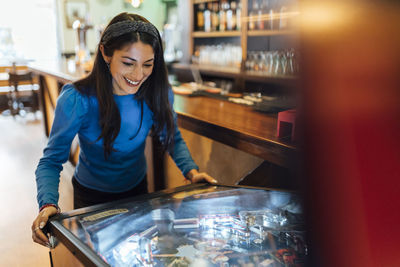 Attractive woman playing pinball in bar