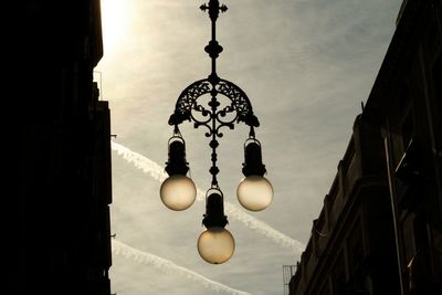 Low angle view of illuminated lighting equipment hanging against sky