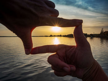 Composition finger frame. girl hands capture in frame sunset above silent lake.