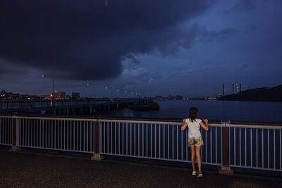 Rear view of man standing by railing against sea