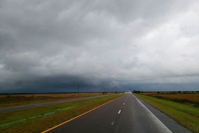 Empty road amidst field against sky