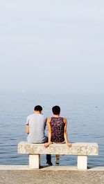 Rear view of friends sitting by sea against sky