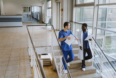 Full length of male doctor and nurse discussing over documents while moving down on staircase in hospital