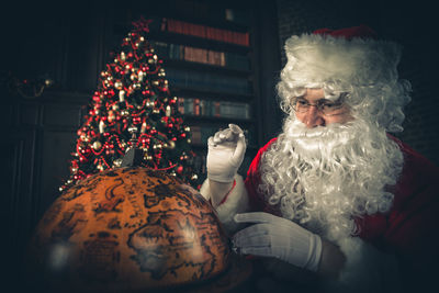 Man wearing santa claus costume looking at globe at home