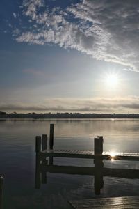 Wooden posts in lake against sky during sunset