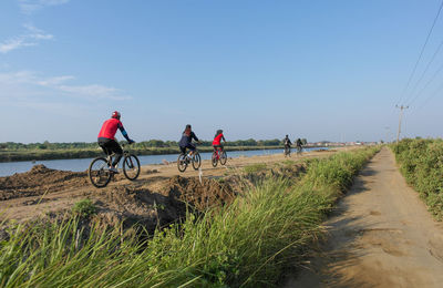 People riding bicycle on grass against sky