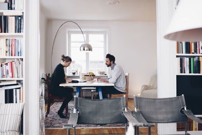 Side view of couple sitting at dining table working from home