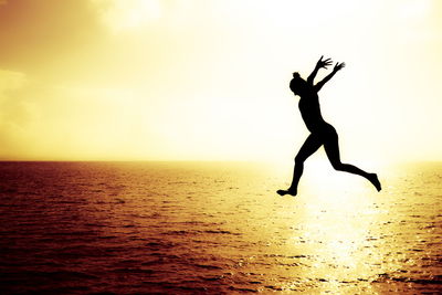 Silhouette woman jumping in sea against sky during sunset