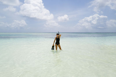 Woman standing in the water wearing wetsuit holding snorkeling equipment