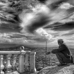 Silhouette of girl sitting against cloudy sky