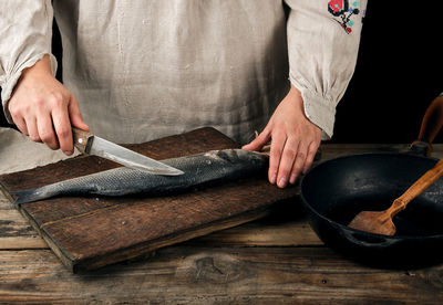 Midsection of woman cutting fish on board in kitchen