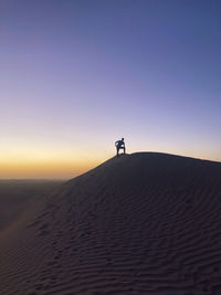 Man on sand dune in desert against clear sky