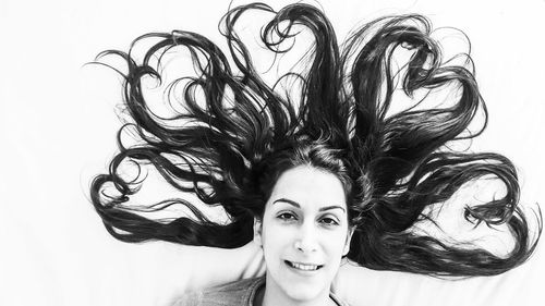 Portrait of happy woman with tousled hair making heart shapes lying on bed