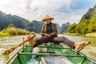 Portrait of female rower sailing on boat in river against sky