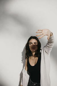 Beautiful woman shielding eyes while standing against white wall