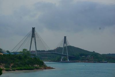 Suspension bridge over sea against cloudy sky