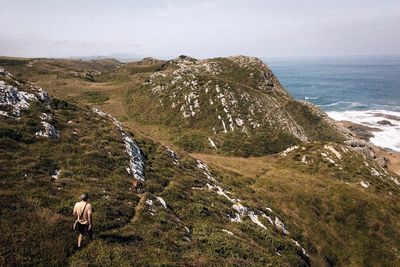 Rear view of man with dog hiking on mountain against sky