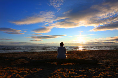 Rear view of woman sitting on beach during sunset