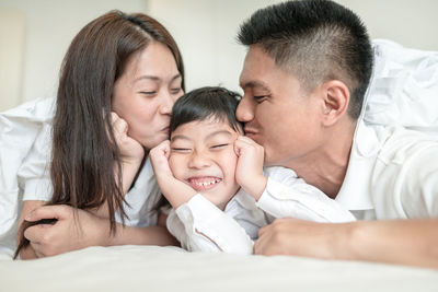 Mother and father kissing boy while lying on bed at home
