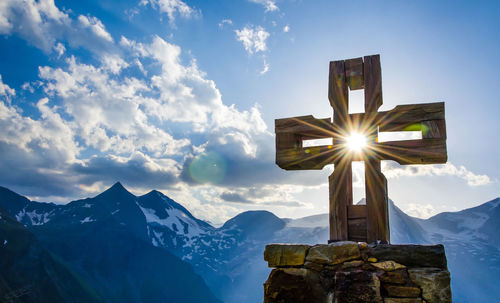 Low angle view of sunlight streaming through summit cross at alps