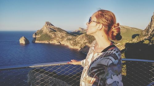 Side view of mid adult woman standing by railing against clear sky