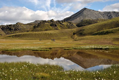 People walking in meadow against cloudy sky