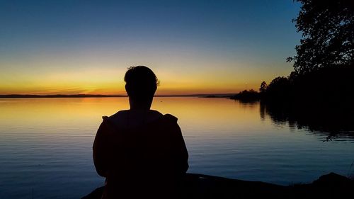 Silhouette man looking at lake against sky during sunset