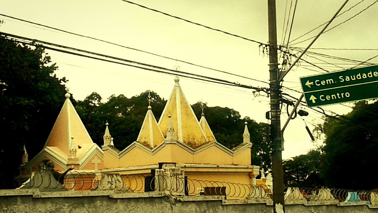 building exterior, architecture, built structure, power line, cable, text, communication, sky, yellow, tree, clear sky, religion, western script, outdoors, place of worship, electricity pylon, church, transportation, low angle view, non-western script