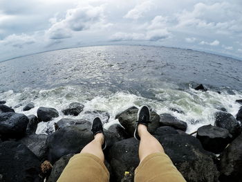 Fish eye view of person on rock by sea against cloudy sky