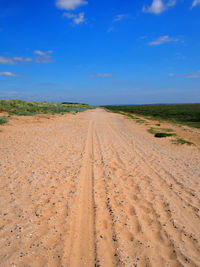 Dirt road on field against sky