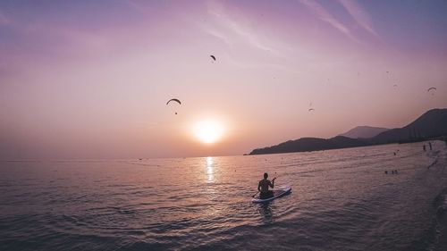 Silhouette people on sea against sky during sunset