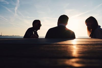 People sitting on beach against sky during sunset